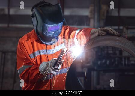 Industrial worker with protective mask welding metal pipe in a factory Stock Photo