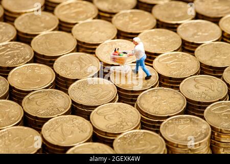 Closeup miniature man with shopping cart placed on stacks of 20 cent euro coins Stock Photo