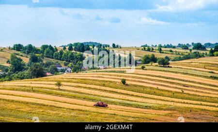 Beautiful view on an agricultural field in the time of harvest. Flat hills, trees on the horizon. Harvester machine in the foreground. Sunny, summer d Stock Photo