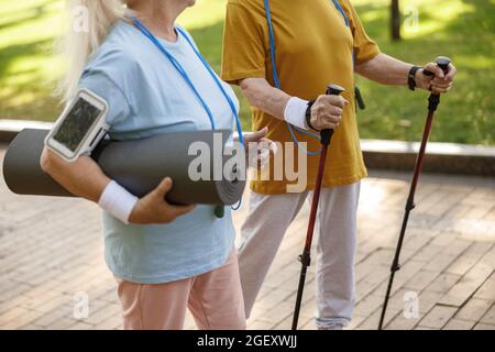Couple of senior people with different sports equipment walk along green city Stock Photo