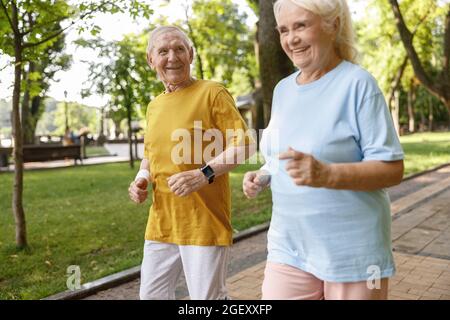 Mature man runs with pretty sportive wife along road in green park in summer Stock Photo