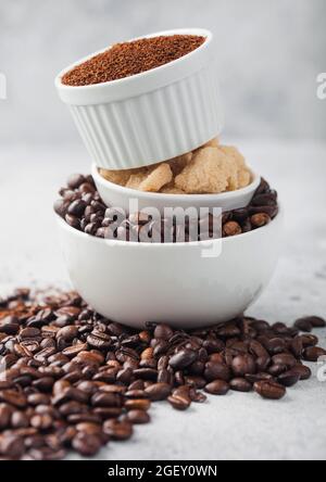 Three bowls on top of each other with fresh raw coffee beans and powder with cane sugar on light table background. Stock Photo