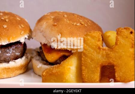 foreground mini hamburgers accompanied by french fries in the shape of letters. Stock Photo