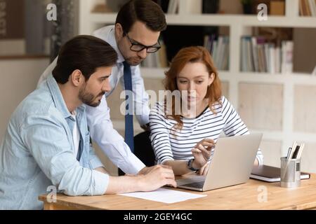 Three caucasian colleagues using laptop discussing collaborative on-line project Stock Photo