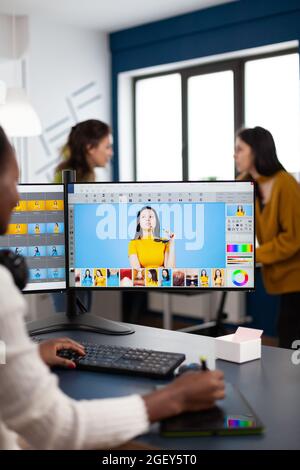 Black retoucher artist analysing images on pc with two monitors and retouching digital assets with stylus pencil. African designer using photo editing software working in creative production office Stock Photo