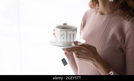 Closeup female hands holding cup with teabag inside Stock Photo