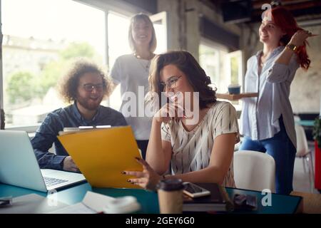group of young people working together. female colleague showing folder to other members of team, smiling Stock Photo