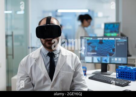 Chemist researcher analyzing sickness development using virtual reality headset during medical experiment in biochemistry hospital laboratory. Modern biotechnology equipment Stock Photo