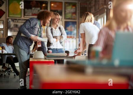 group of people gathered around the table, standing, smiling, talking, laughing, having fun at work. Stock Photo
