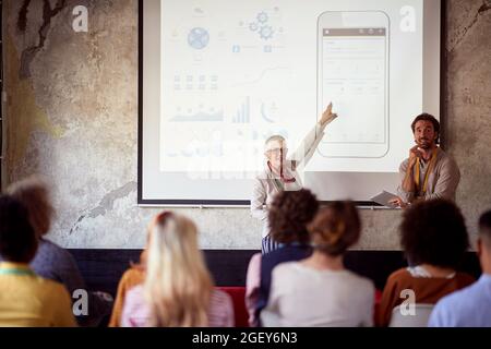 elderly caucasian female lecturing students together with her male assistant, showing, explaining Stock Photo