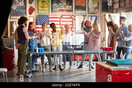 fun and teambuilding at work concept. group of multiethnic employees having break at work, playing beer pong. Stock Photo