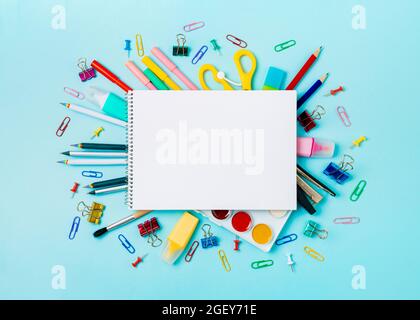 Notebook with stationary objects on blue background. Empty white paper sheet of notepad or sketchbook over shool supplies, isolated on blue. Copy space for text or design. Top view, flat lay Stock Photo