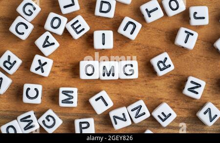 Small white and black bead cubes on wooden board, letters in middle spell OMG. Stock Photo