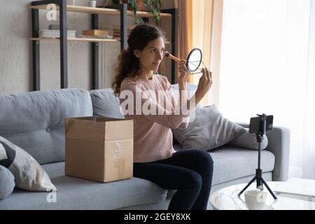 Woman apply powder on face records vlog on cellphone Stock Photo
