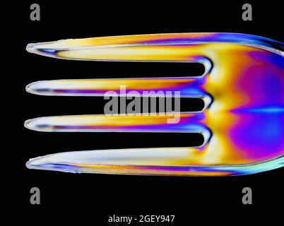 Colourful patterns form on a clear plastic fork caused by the refraction of polarised light Stock Photo