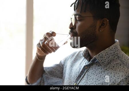 Peaceful millennial Afro American guy drinking water with closed eyes Stock Photo