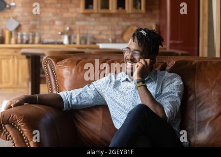 Happy thoughtful millennial Black hipster guy speaking on mobile phone Stock Photo