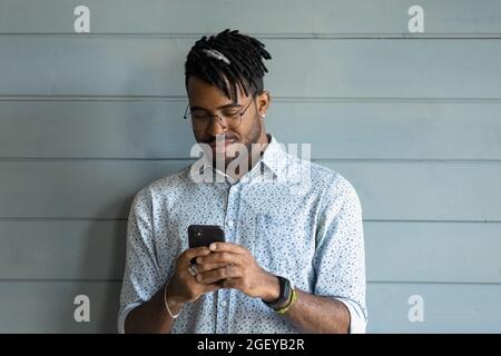 Happy handsome millennial African guy texting message on mobile phone Stock Photo