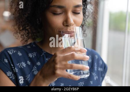 Peaceful smiling young African American woman drinking pure filtered water Stock Photo