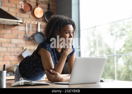 Thoughtful female African American remote employee standing by computer Stock Photo