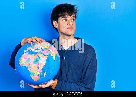 Handsome hipster young man holding world ball smiling looking to the side and staring away thinking. Stock Photo