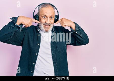 Handsome senior man with beard listening to music using headphones smiling cheerful showing and pointing with fingers teeth and mouth. dental health c Stock Photo