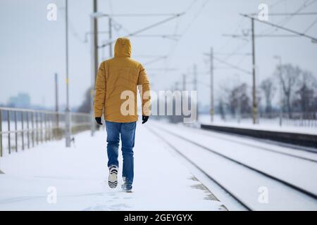 Rear view of loneliness person in warm clothing. Man leaves train station against snowy landscape. Stock Photo