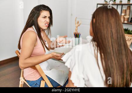 Two latin paint students arguing sitting on the table at art school. Stock Photo