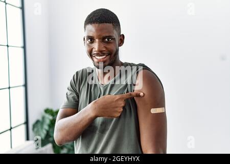 Young african american man getting vaccine showing arm with band aid smiling happy pointing with hand and finger Stock Photo
