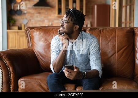 Thoughtful millennial African guy with mobile phone looking at window Stock Photo