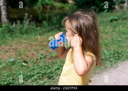 07.11.2021 Moscow, Russia A little girl in a yellow T-shirt drinks Pepsi Cola on a hot summer day Stock Photo