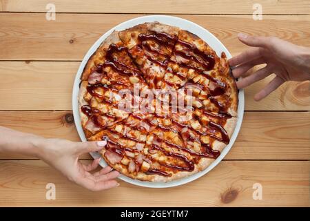 Pizza dining. Two hands taking slices on top of wooden table, overhead shot Stock Photo