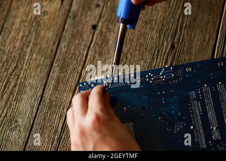 Technician or engineer is focused on repairing electronic circuit board with soldering iron. Man hands soldiers computer circuit board using soldering Stock Photo