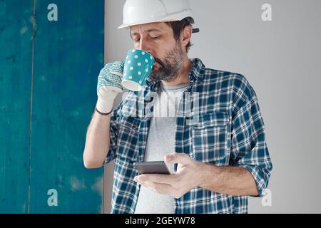 Construction engineer on a morning coffee break using mobile phone, relaxing and preparing for work Stock Photo