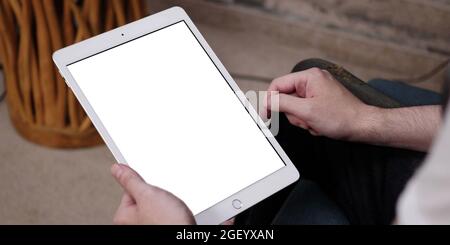 A tablet with white empty screen, close up on man's hands while holding an apple iPad with blank touchscreen. Stock Photo