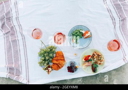 Photo from above of beautiful summer picnic details on white linen tablecloth, croissant, fresh fruits and plate with salad, different types of sandwi Stock Photo