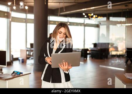 Confident businesswoman CEO female checking emails online, doing job on laptop while walking on office meeting, smiling lady executive typing message, Stock Photo