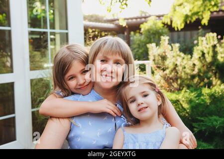 Happy loving middle-aged grandma hugging  granddaughters while standing in garden on summer day, grandmother with small girls spending time together i Stock Photo