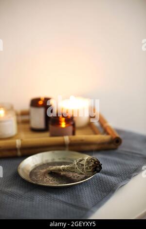 Incense for fumigation, branches of white sage tied in bunch with dried flowers, aroma smudge stick burning on metal plate, aromatherapy and meditatio Stock Photo