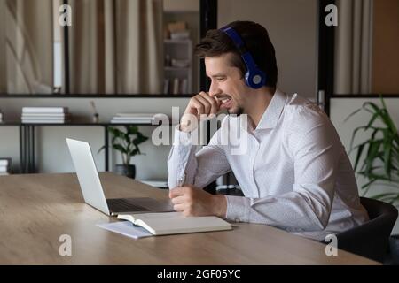 Happy male employee work distant on laptop taking notes Stock Photo