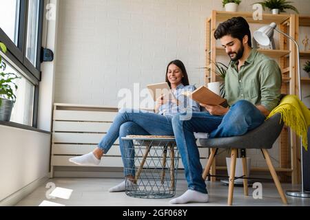 Free time together. Happy couple is spending weekend together at home. Reading book, tablet. Stock Photo