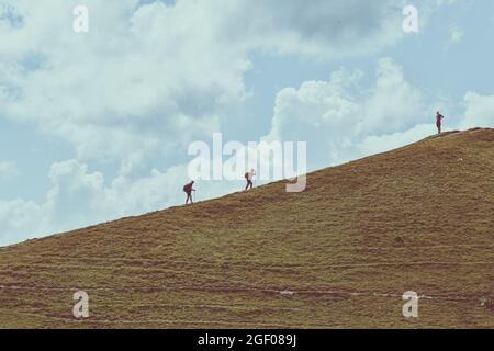 Man and woman climbing up a hill. Their friend is waiting for them at the top. Mountain hiking. Teamwork concept. Motivational background Stock Photo