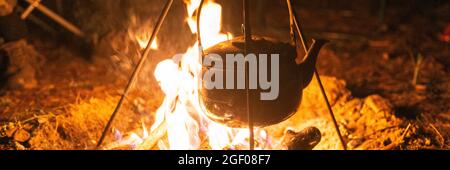 Campfire kettle closeup with blurred bonfire in the background