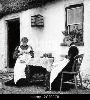 An early 20th century scene of two women making Carrickmacross Lace outside their thatched cottage in County Monaghan. It was introduced into Ireland in about 1820 by one Mrs Grey Porter of Donaghmoyne, who taught it to local women so that they could earn some extra money. Porter had been inspired by some examples of appliqué lace she had seen while on her honeymoon in Italy. Stock Photo