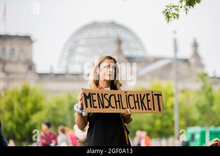 Berlin, Germany. 22nd Aug, 2021. A woman holds a sign reading 'Humanity' in front of the German Chancellery during a demonstration by a broad alliance for the admission of people from Afghanistan, with the Reichstag building in the background. (has agreed) Credit: Christoph Soeder/dpa/Alamy Live News Stock Photo