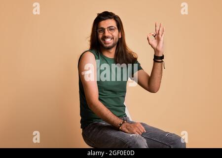 Cheerful indian guy showing okay, got vaccinated against COVID-19 Stock Photo