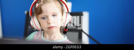 Little girl in headphones sits in front of monitor with microphone Stock Photo