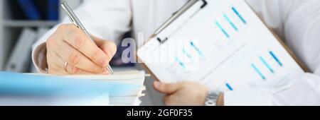 Businessman holds clipboard with commercial charts in his hands and makes notes in documents Stock Photo