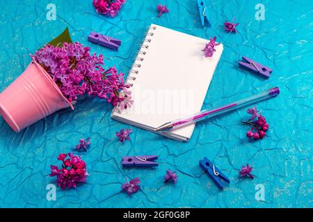 Blank notebook, pen with purple ink and lilac flowers on vintage painted blue cardboard background Stock Photo