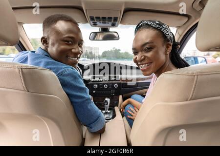 Happy afro american couple posing in auto, looking at backseat Stock Photo